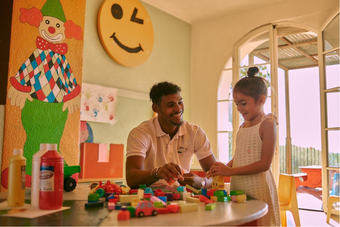 Enfant accompagné d’un GO devant une table remplie de blocs de construction, jouets et peinture au Club Med Opio en Provence.