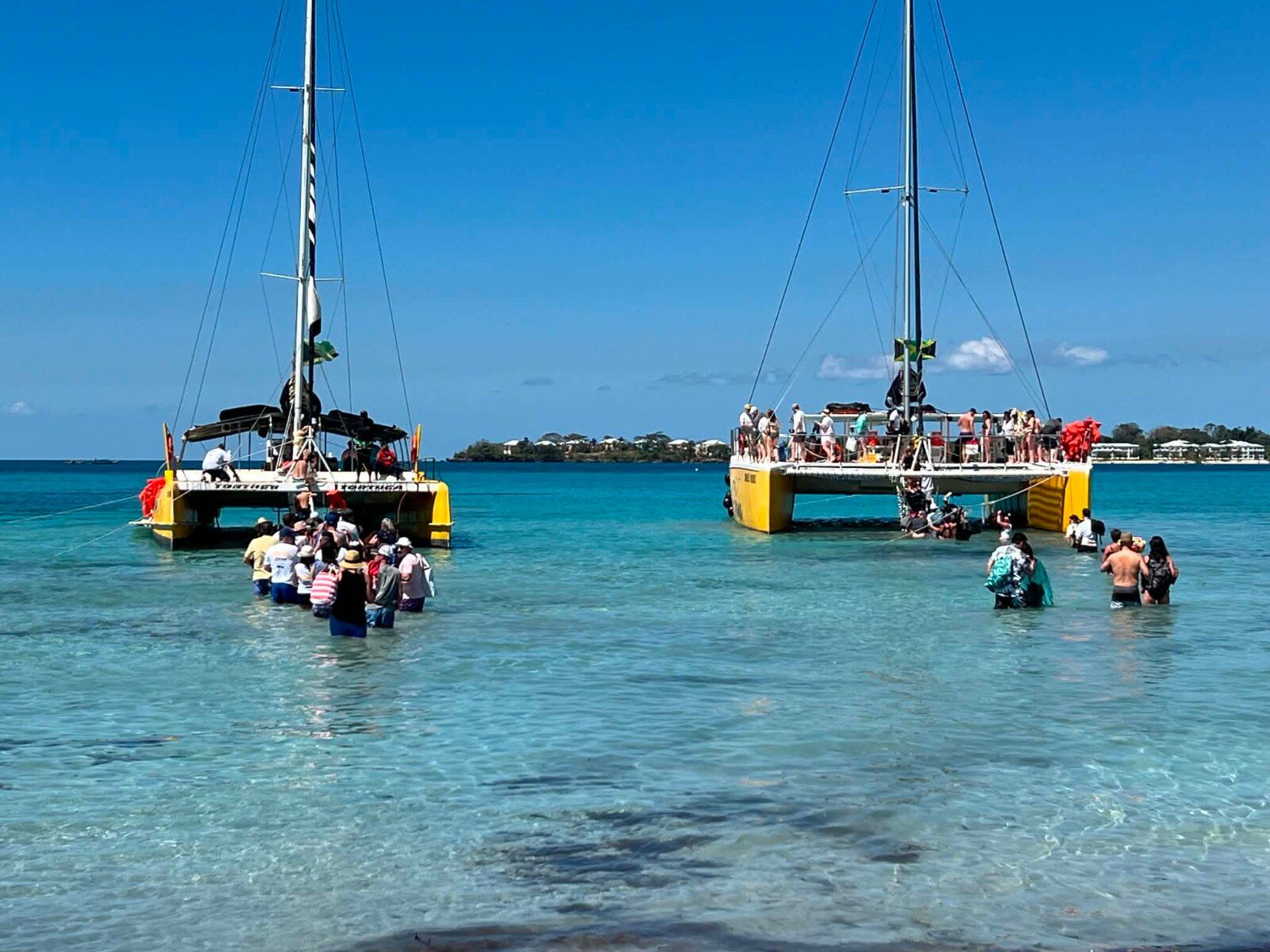 Two catamarans anchored in shallow water, participants boarding from the beach in Negril