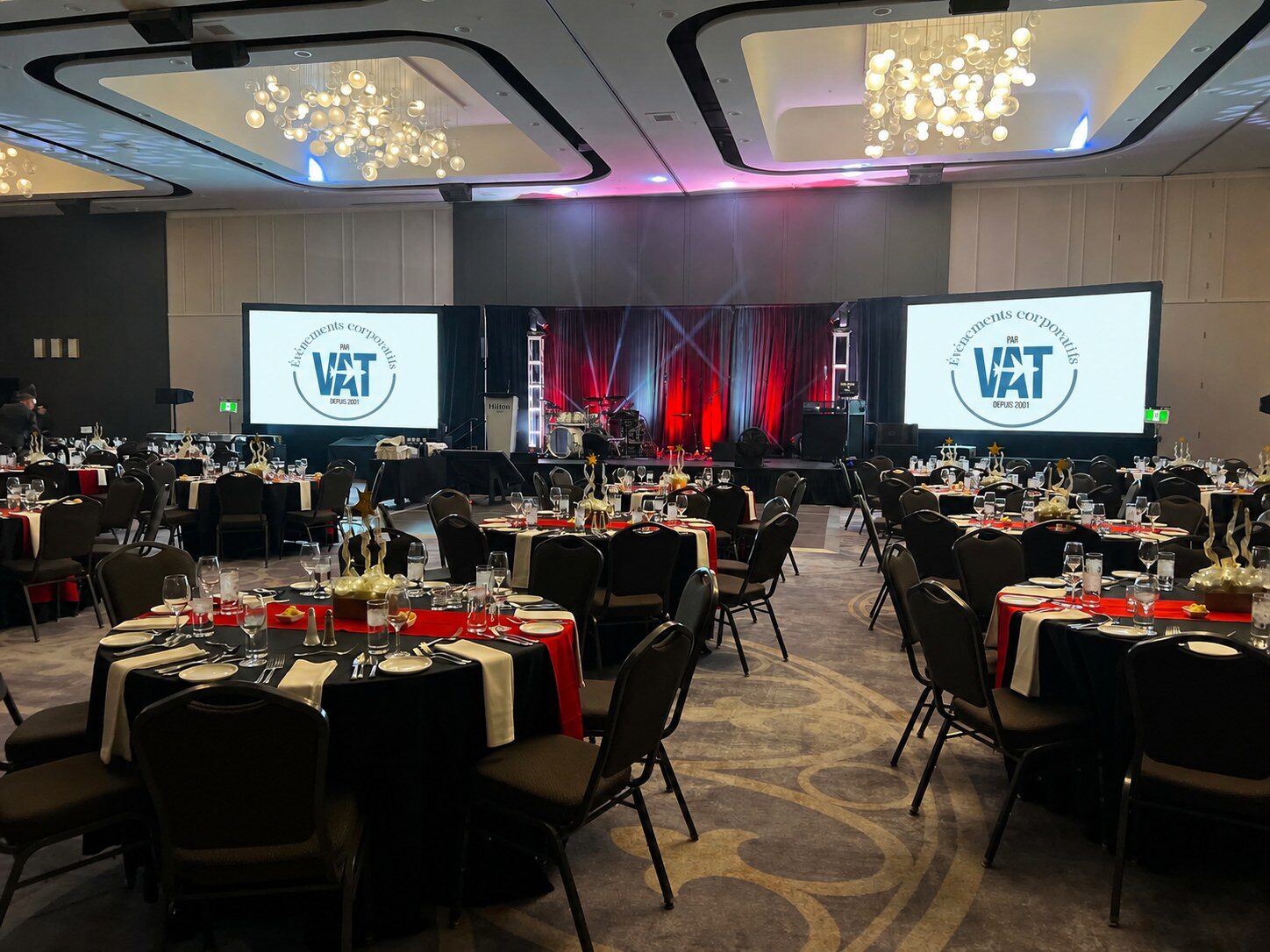 Ballroom set for a corporate gala evening, round tables and two large screens