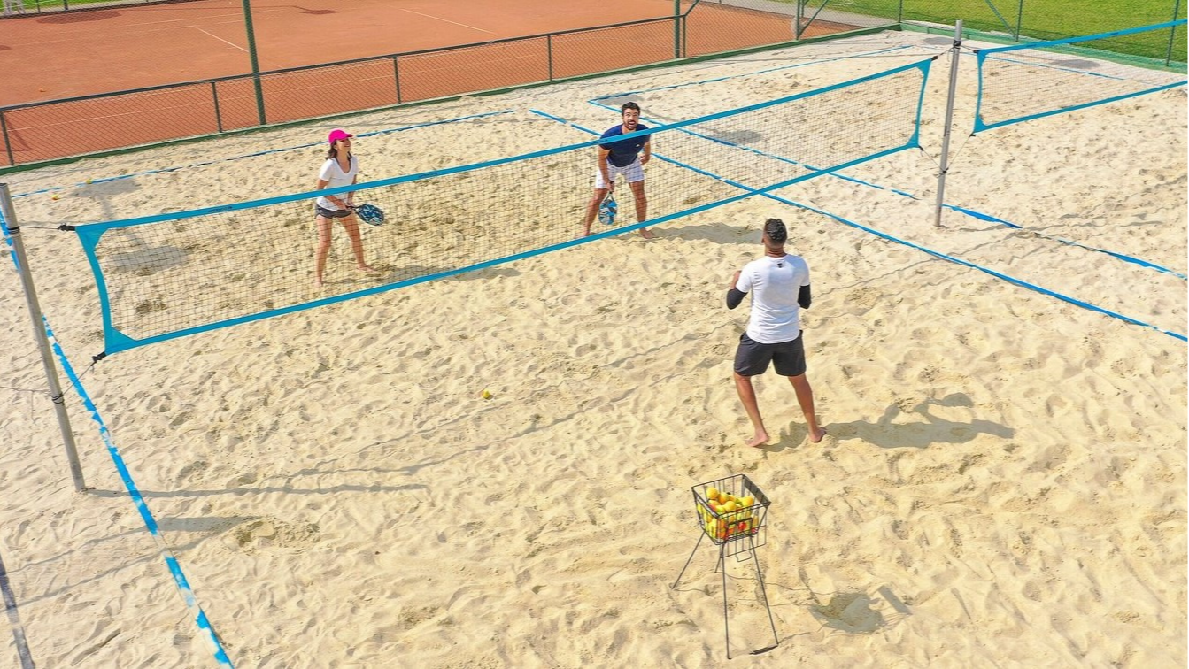 Couple on the beach at Club Med Lake Paradise, Brazil, learning beach tennis with an instructor in a sporty atmosphere.