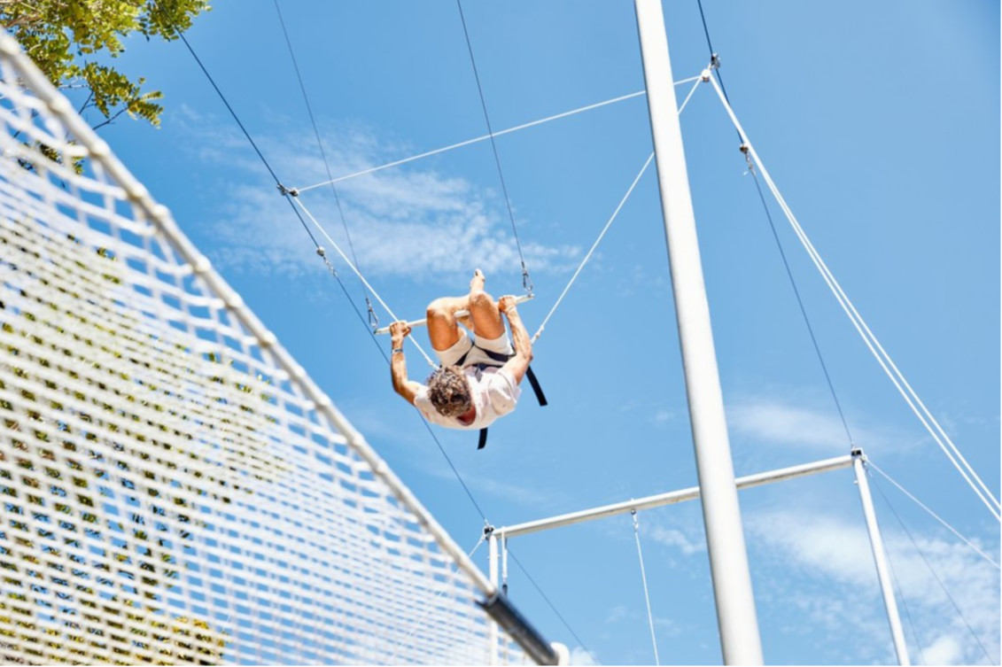 Adult on the trapeze at Club Med Lake Paradise, Brazil, upside down, against a clear sky.