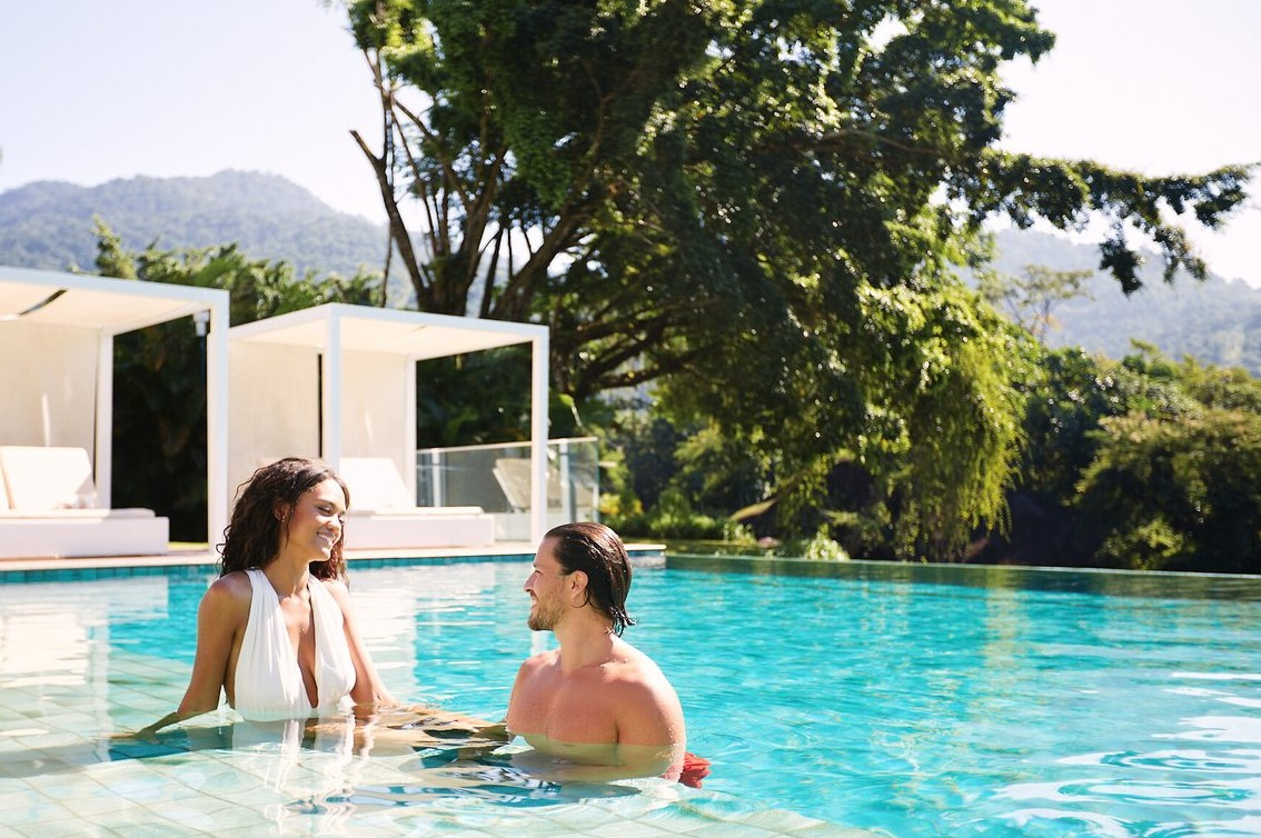 Couple relaxant dans la piscine du Club Med Rio Das Pedras avec des lits de détente sous pergolas en arrière-plan.