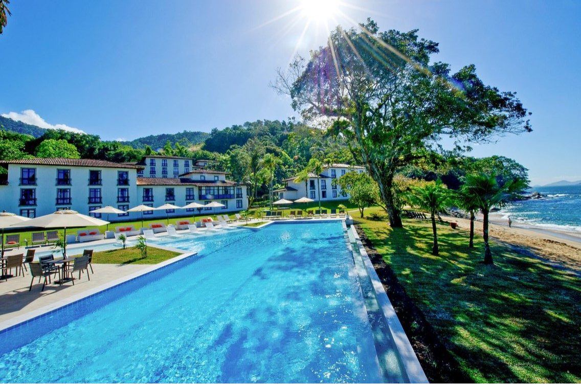 Aerial view of the pool at Club Med Rio Das Pedras with the resort in the background and lounge chairs lined up.