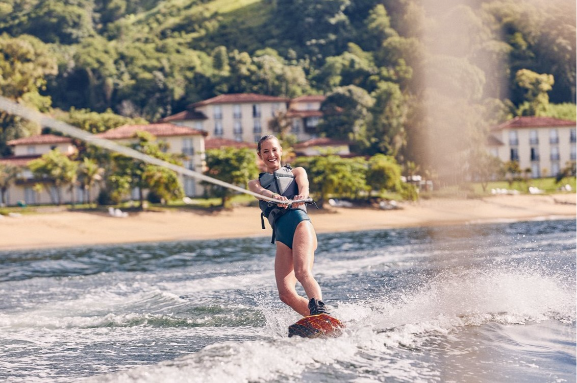 Front view of a woman wakeboarding on the emerald blue waves of the Atlantic at Club Med Rio Das Pedras.