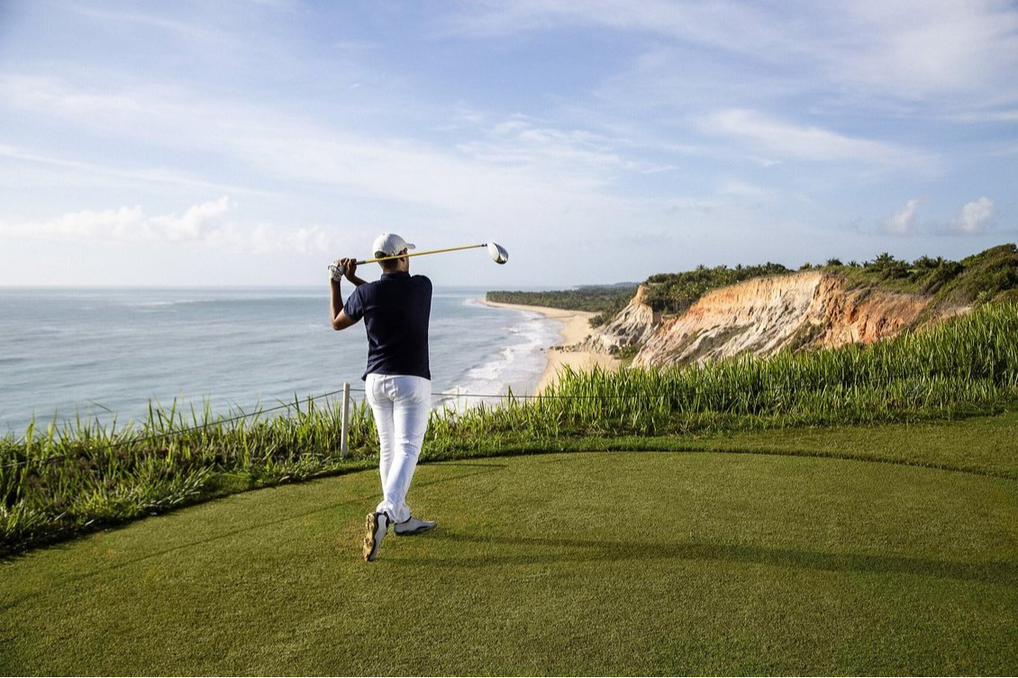 Golfeur frappant une balle sur le parcours du Club Med Trancoso, avec une vue magnifique sur l’océan Atlantique.