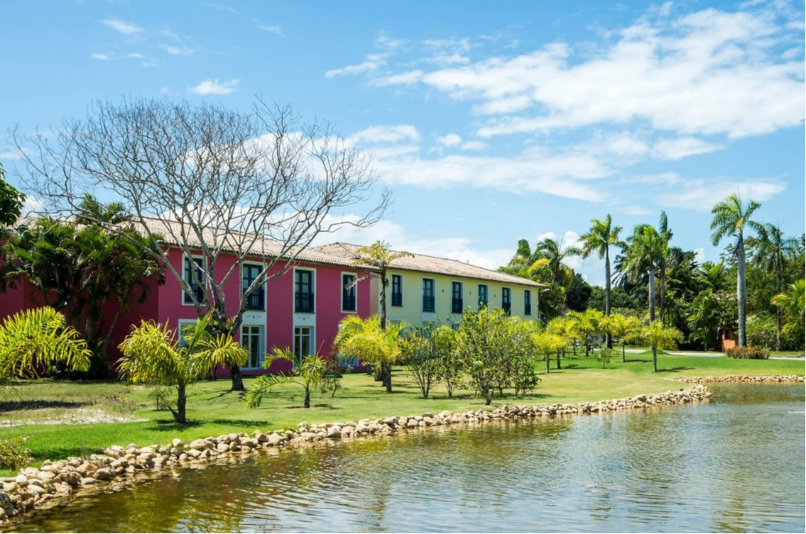 Vue du complexe Club Med Trancoso au Brésil, avec lac bordé de roches et palmiers, offrant un cadre naturel idyllique.