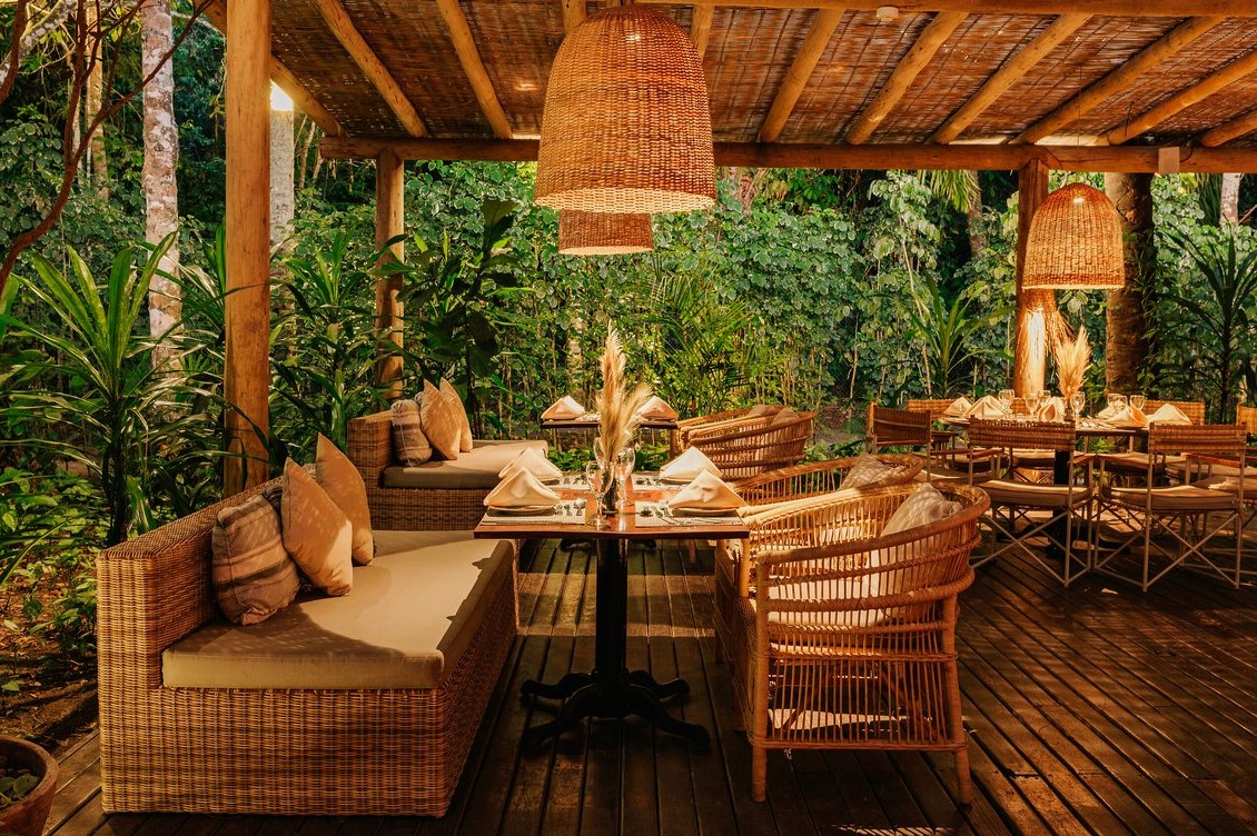 Covered terrace of Lua restaurant at Club Med Trancoso, surrounded by tropical greenery and featuring rattan furniture.