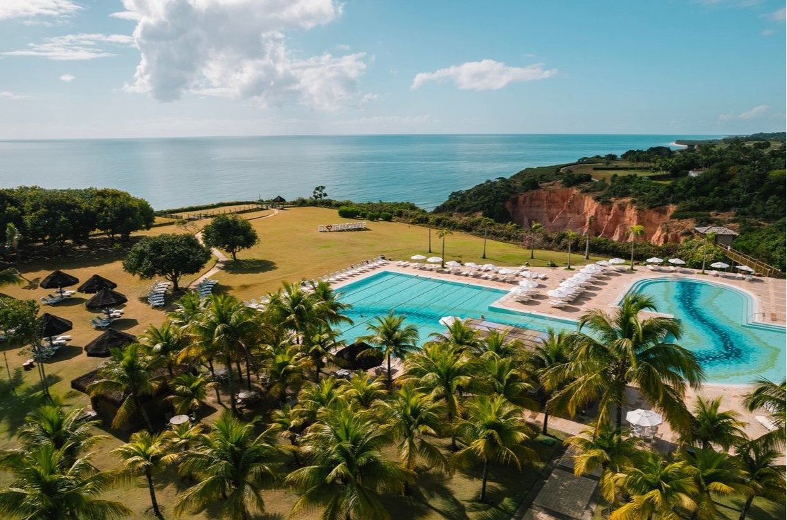 Aerial view of Club Med Trancoso with a pool and ocean backdrop, surrounded by palm trees and lush greenery.