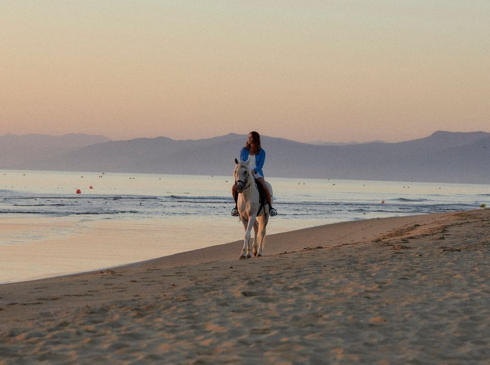 Femme se promenant à cheval sur la plage du Club Med Yasmina, dans un décor spectaculaire de coucher de soleil.