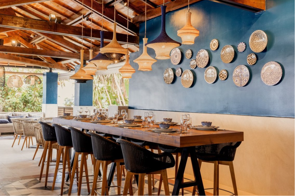 Bistro-style table with ten chairs at Club Med Yasmina, adorned with decorative plates on the wall and a wooden roof.