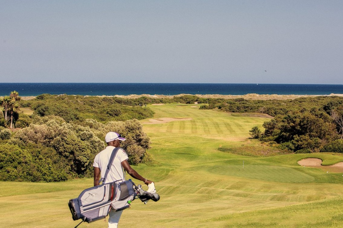 Golfeur transportant son sac au Club Med Yasmina, sur un terrain avec vue sur la Méditerranée.