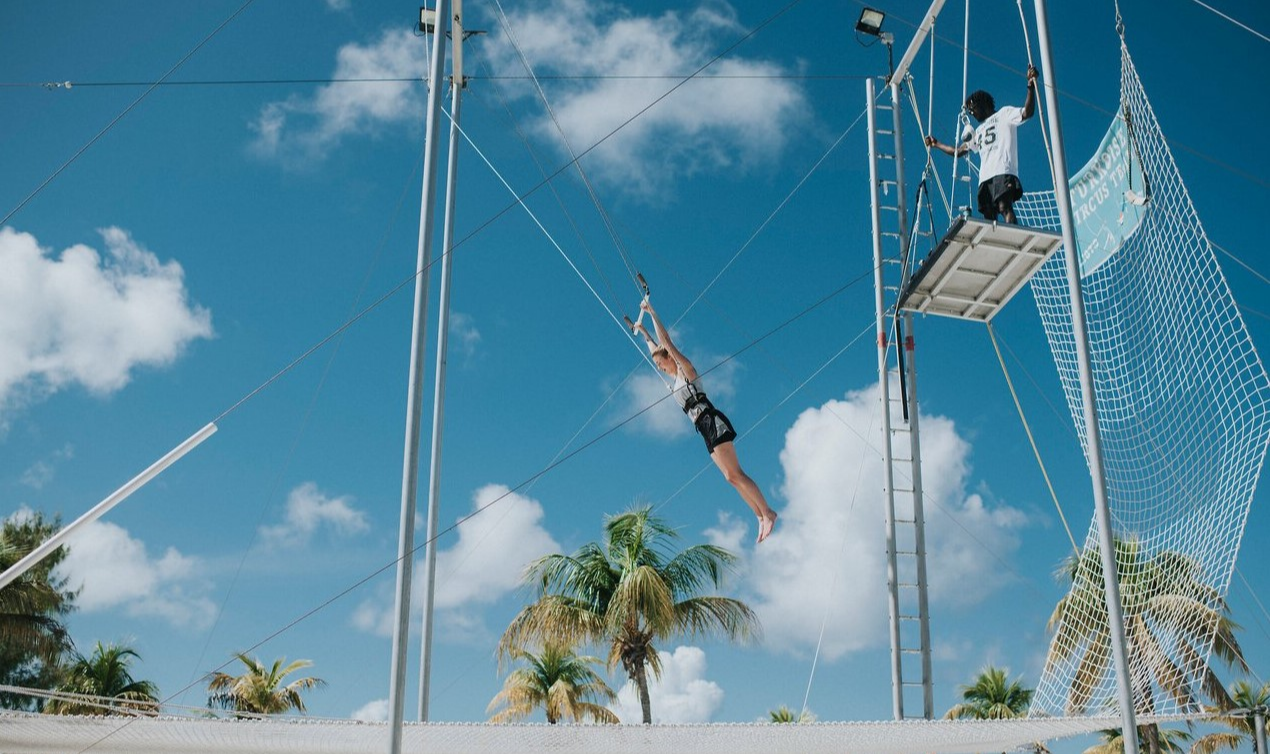 Woman trying the trapeze at Club Med Yasmina, guided by an instructor for a fun and dynamic activity.