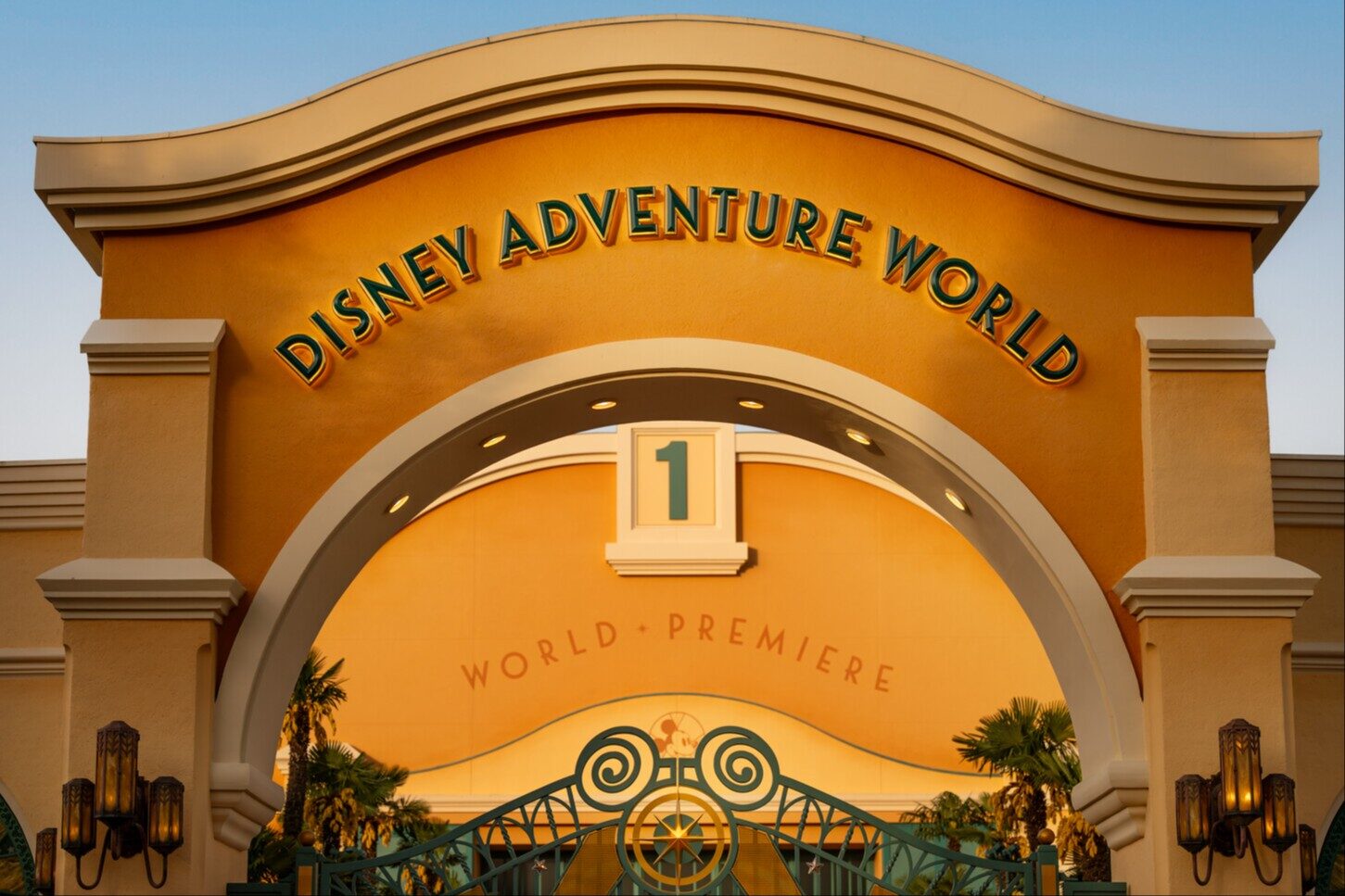 L'arche d'entrée de Disney Adventure World, dorée par le soleil, avec le nom du parc en lettres en relief. Photo : ©Disney.