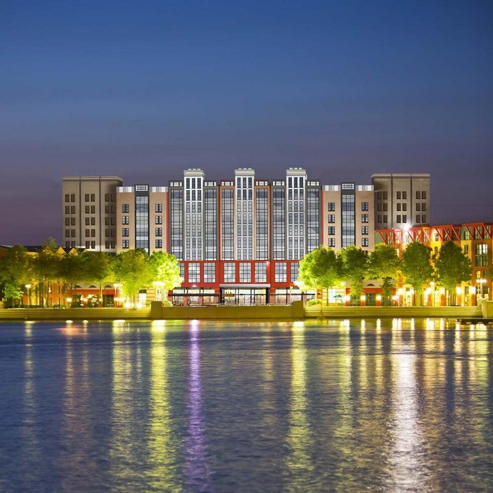 La façade du Disney Hotel New York – The Art of Marvel à la tombée du jour, avec ses gratte-ciel illuminés qui se reflètent dans le lac Disney. Photo : ©Disney.