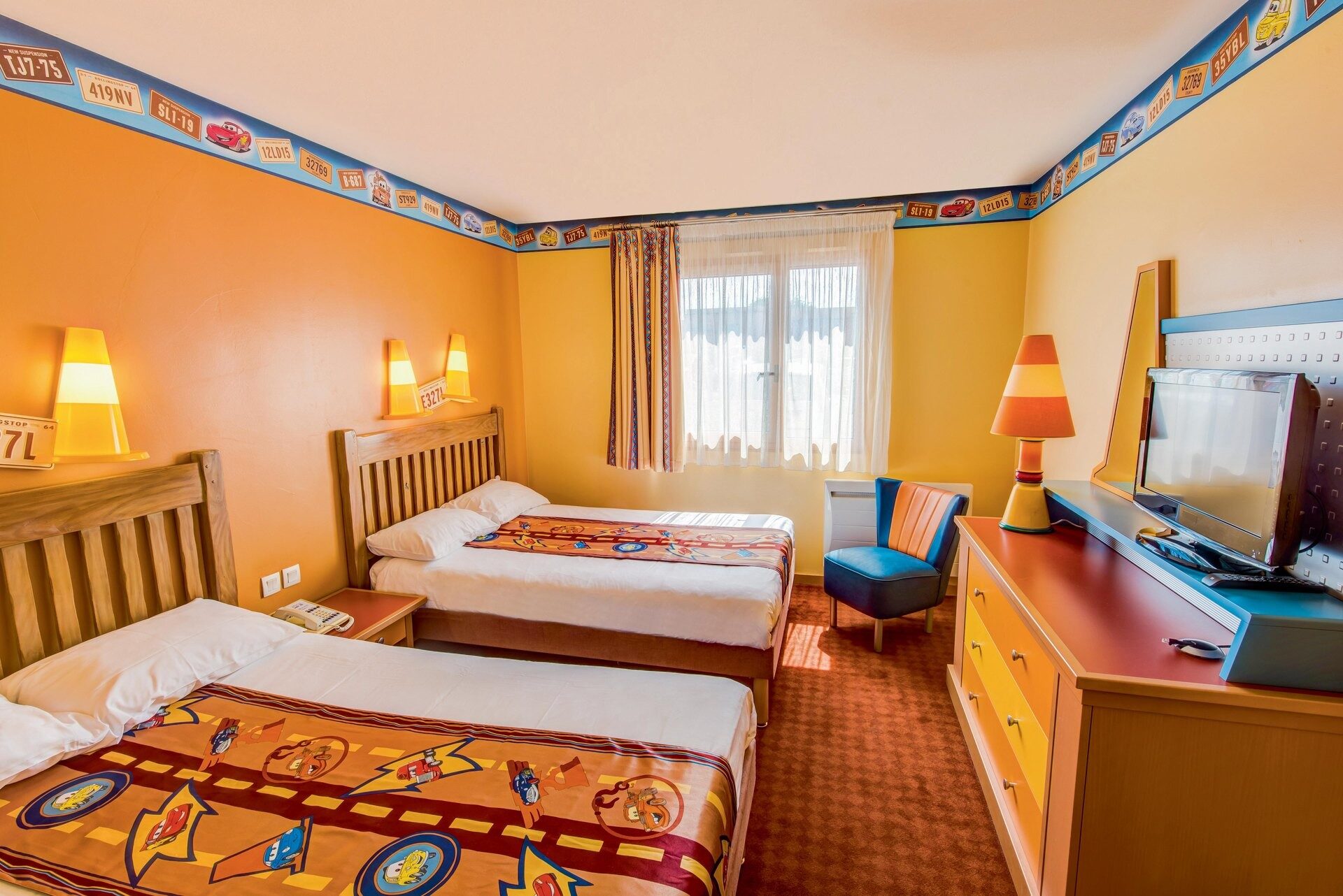 Une chambre du Disney Hotel Santa Fe, avec deux grands lits, des murs jaune soleil et une frise colorée inspirée de la route. Photo : ©Disney/Pixar.