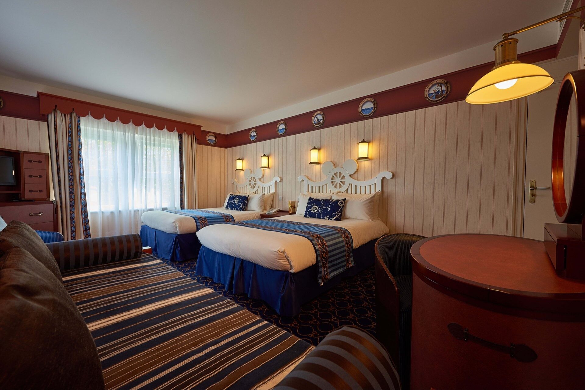 Une chambre du Disney Newport Bay Club, avec deux grands lits aux couvre-lits rayés bleu et blanc et un décor marin de boiseries blanches. Photo : ©Disney.
