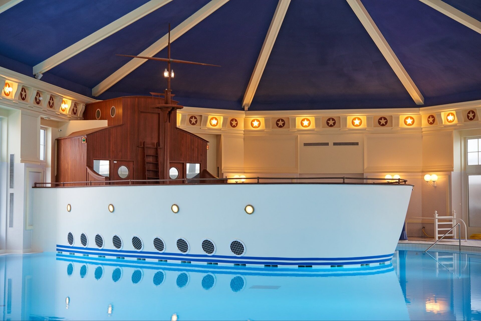 La piscine intérieure du Disney Newport Bay Club, dominée par une coque de paquebot blanche percée de hublots. Photo : ©Disney.