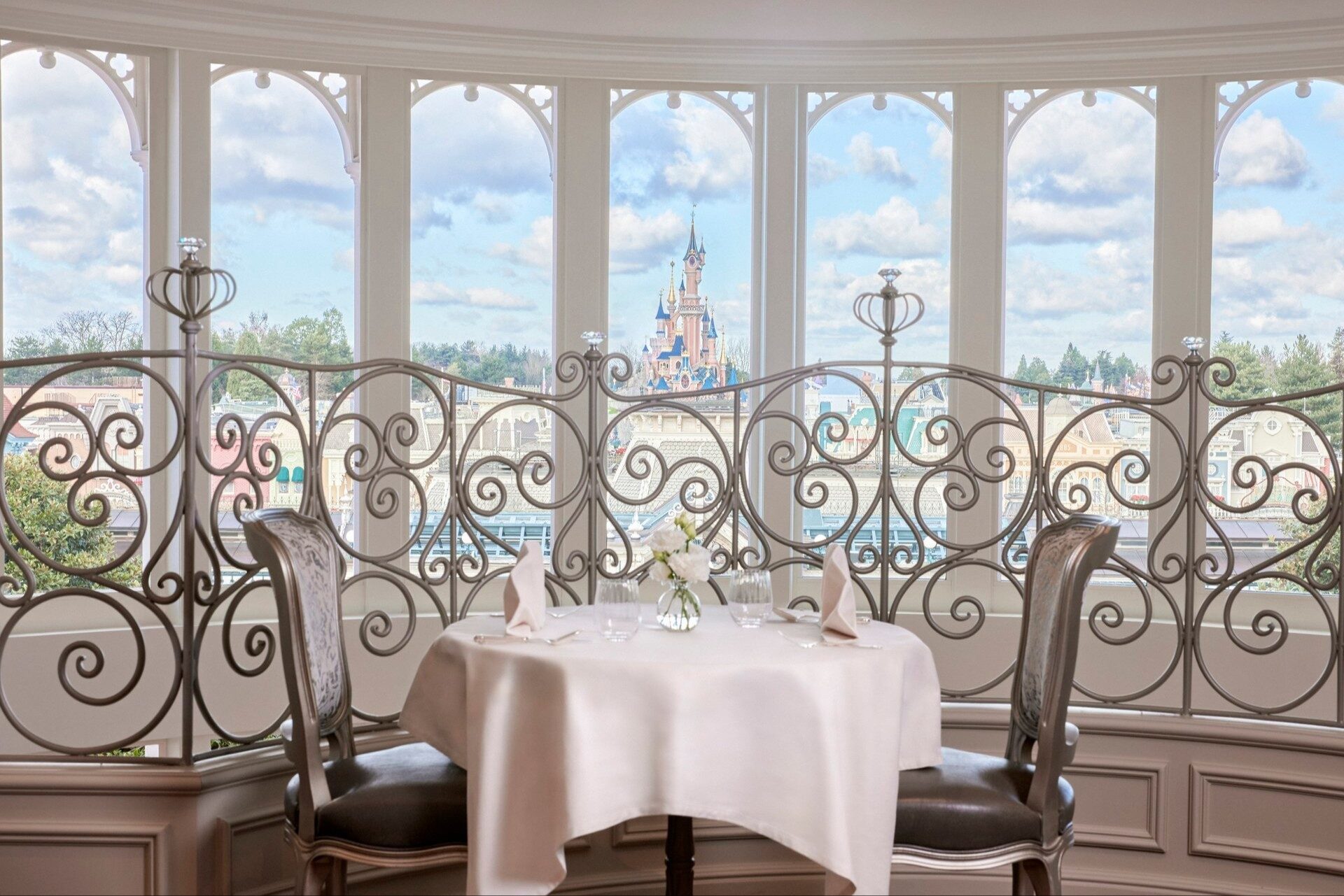 Une table dressée au Castle Club du Disneyland Hotel, derrière une balustrade en fer forgé qui donne sur le Château de la Belle au Bois Dormant. Photo : ©Disney.