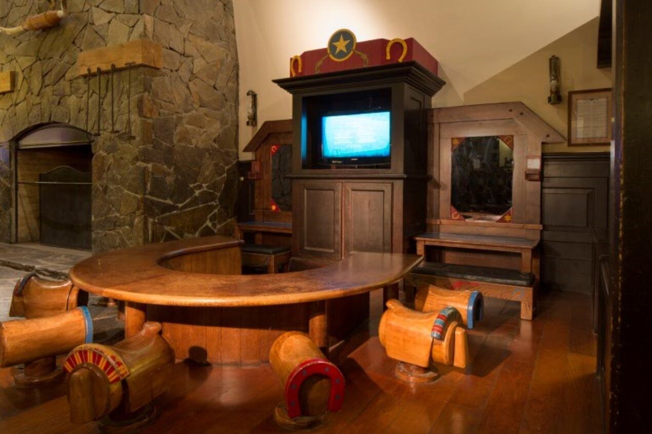 Le coin des enfants du Disney Hotel Cheyenne, avec une table ronde entourée de sièges en forme de chariots, devant une cheminée de pierre.