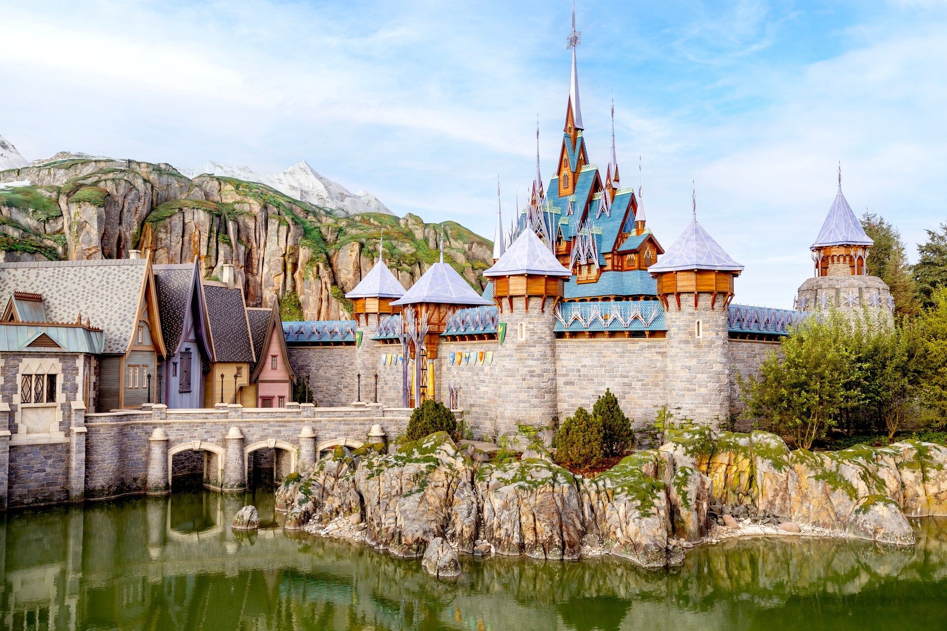 Le château d'Arendelle et le village de World of Frozen, à Disney Adventure World, reflétés dans le lac au pied de la montagne. Photo : ©Disney.