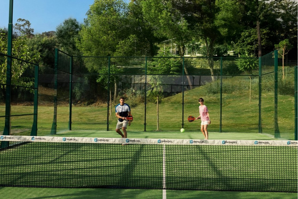 Couple playing padel as a team on a synthetic court surrounded by glass walls at Club Med Opio in Provence.