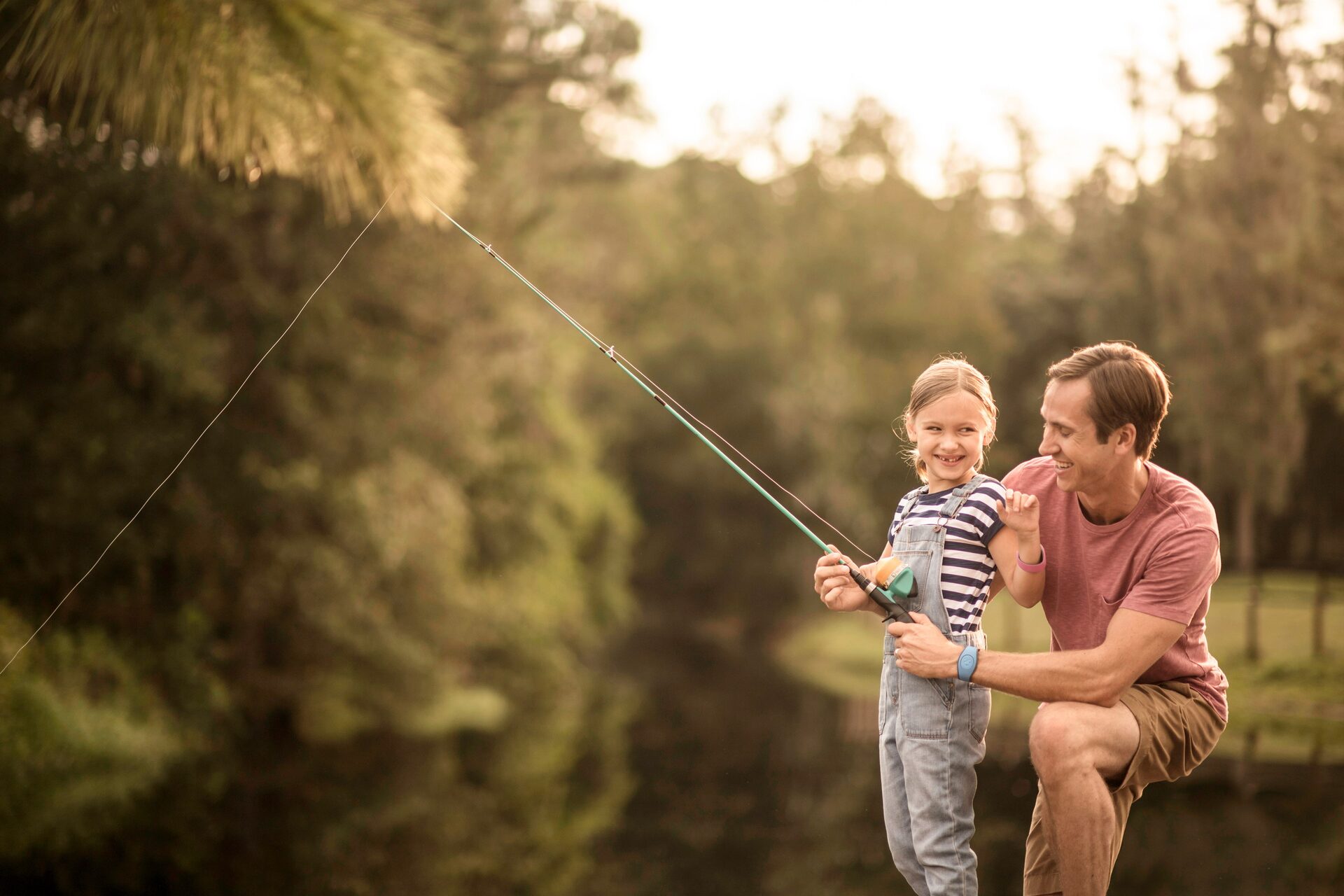 Un père et son enfant lancent leur ligne au bord de l’eau à contre-jour, en fin de journée, à Disney’s Fort Wilderness Resort & Campground. Un père et son enfant lancent leur ligne au bord de l’eau à contre-jour, en fin de journée, à Disney’s Fort Wilderness Resort & Campground.