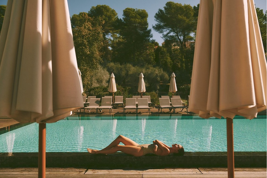 emme au bord de la piscine du Club Med Opio en Provence, entourée de chaises longues, parasols et arbres pour un moment de détente.