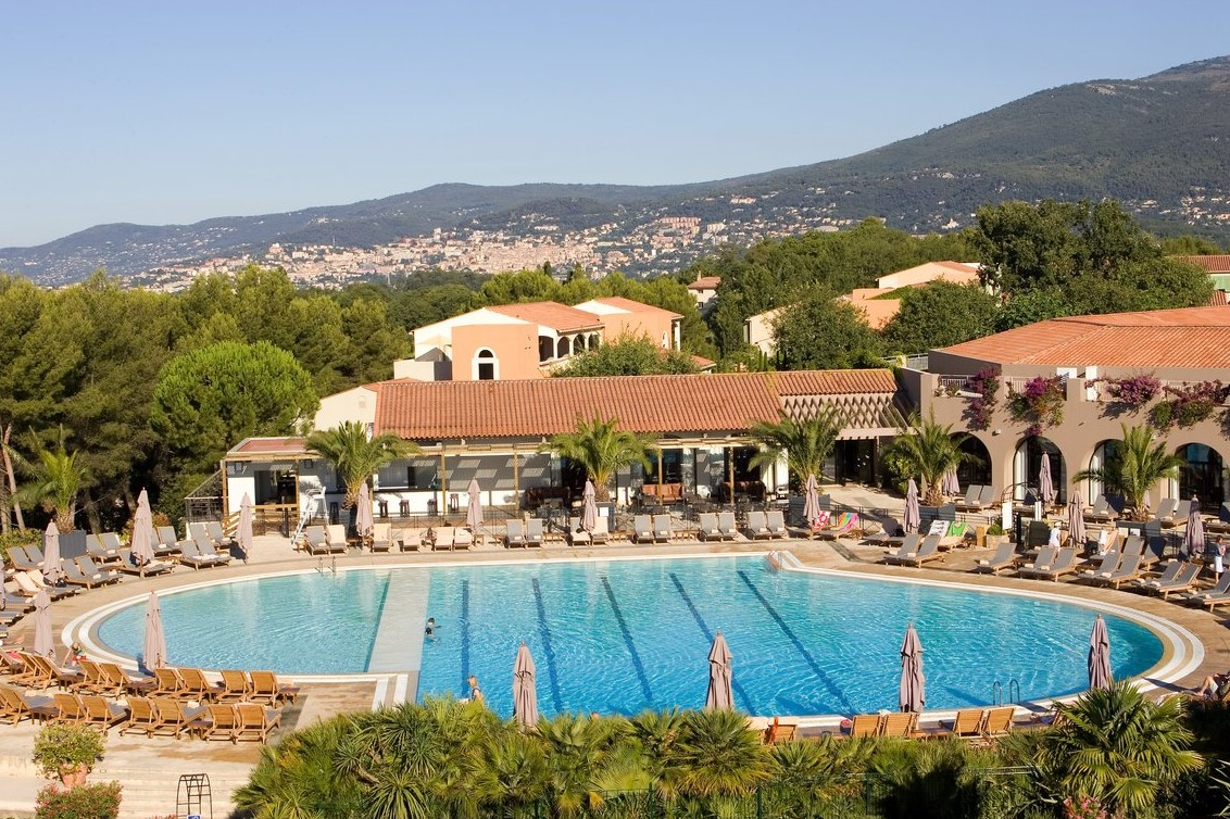 Vue aérienne de la piscine du Club Med Opio en Provence avec le complexe hôtelier en arrière-plan et la ville au loin.